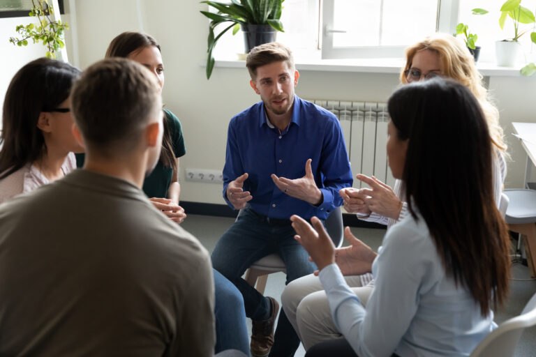 Diverse people seated in circle participating at group therapy session